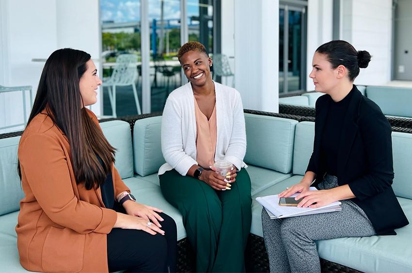 Three professionally-dressed people sitting on an outdoor sofa for a meeting